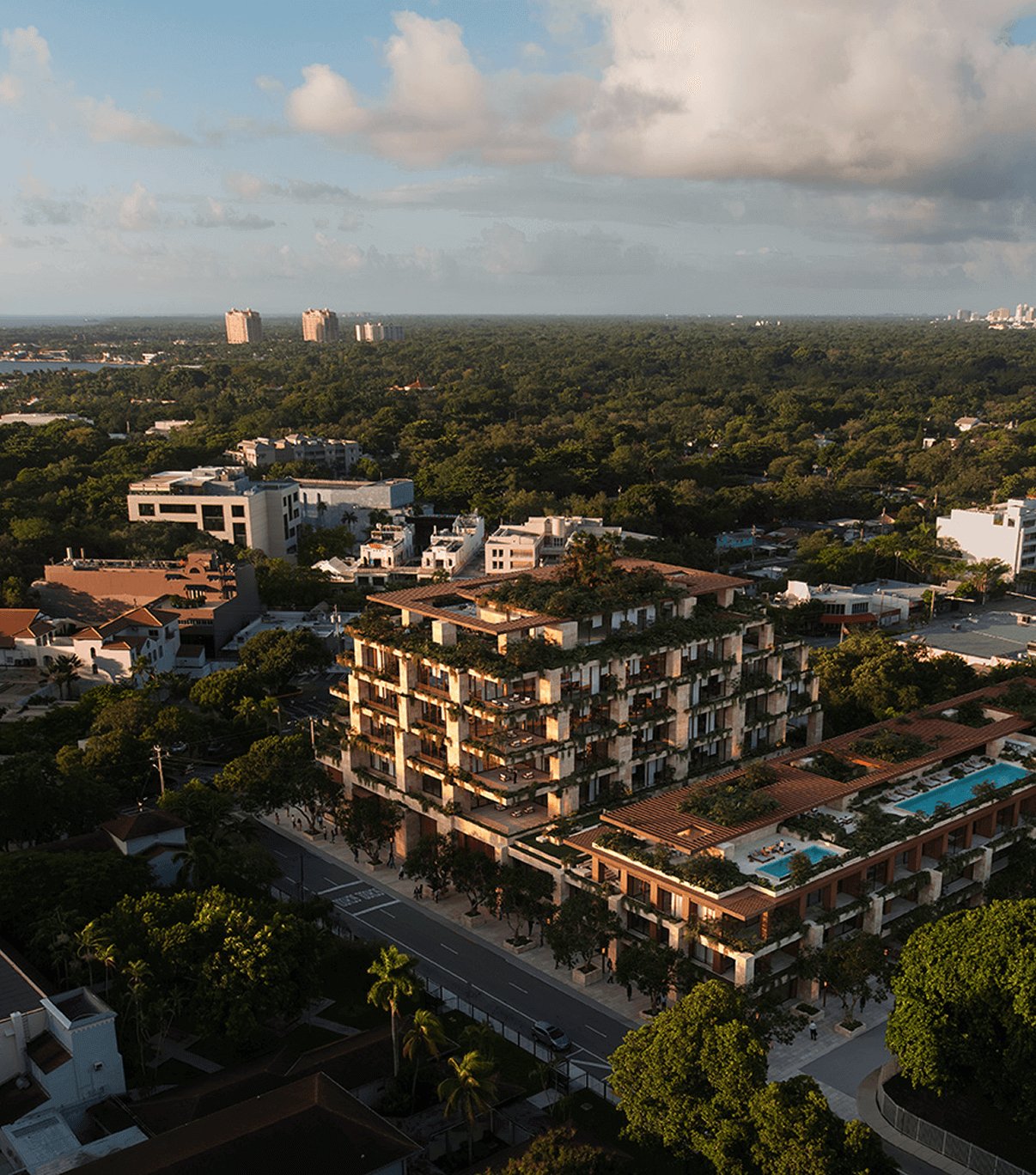 Aerial view of a terraced residential building with rooftop greenery and pools amid a tree-filled neighborhood.