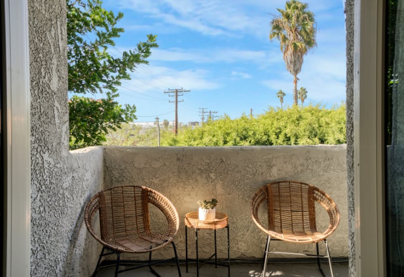 Stucco balcony with two woven chairs and a view of trees and a palm.