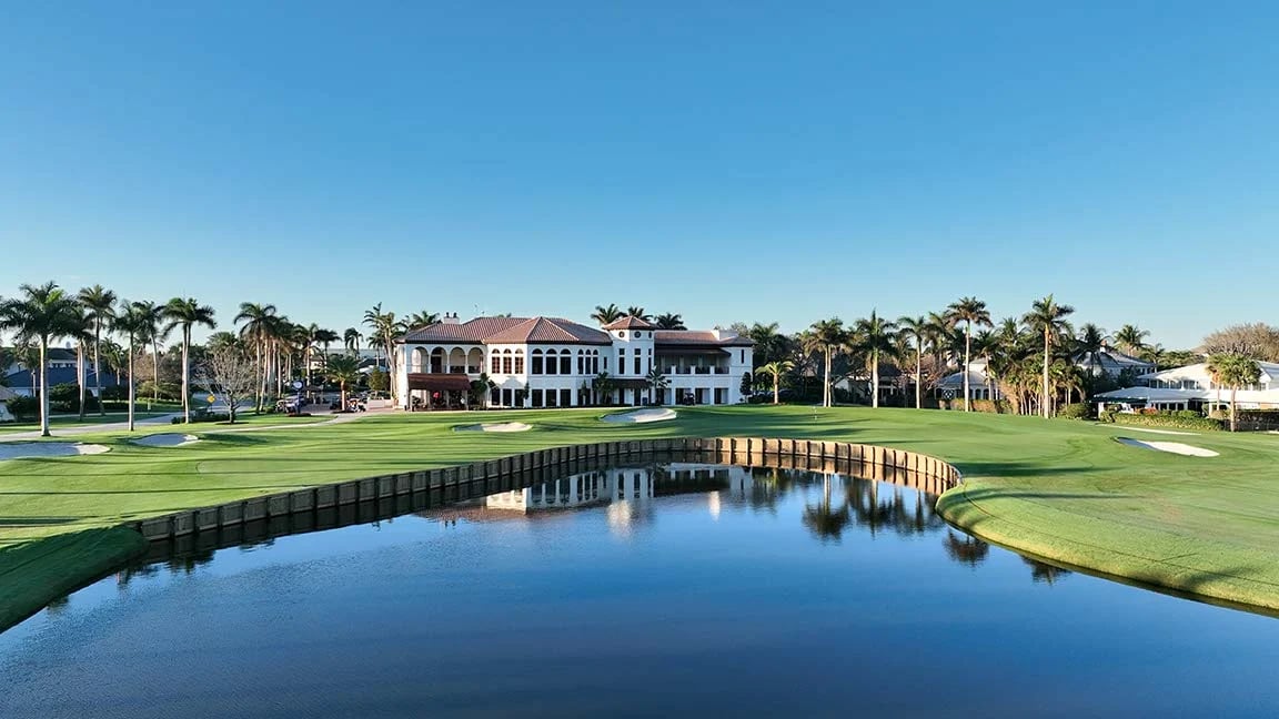 Golf course and pond in front of a palm-lined country club clubhouse.