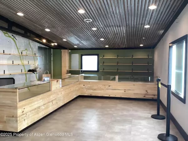 Empty retail space with a long wood counter, wall shelving, and a corrugated metal ceiling.
