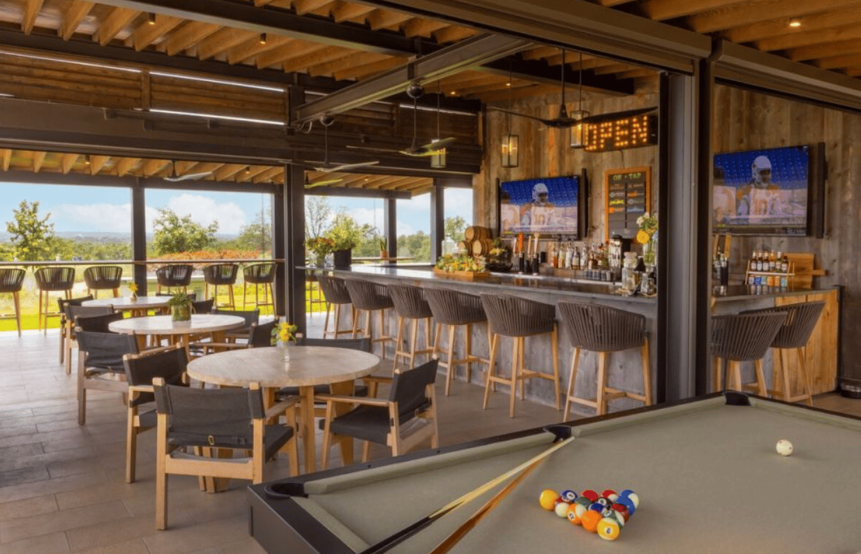 Clubhouse bar and lounge with a pool table, dining tables, and open views of green grounds.