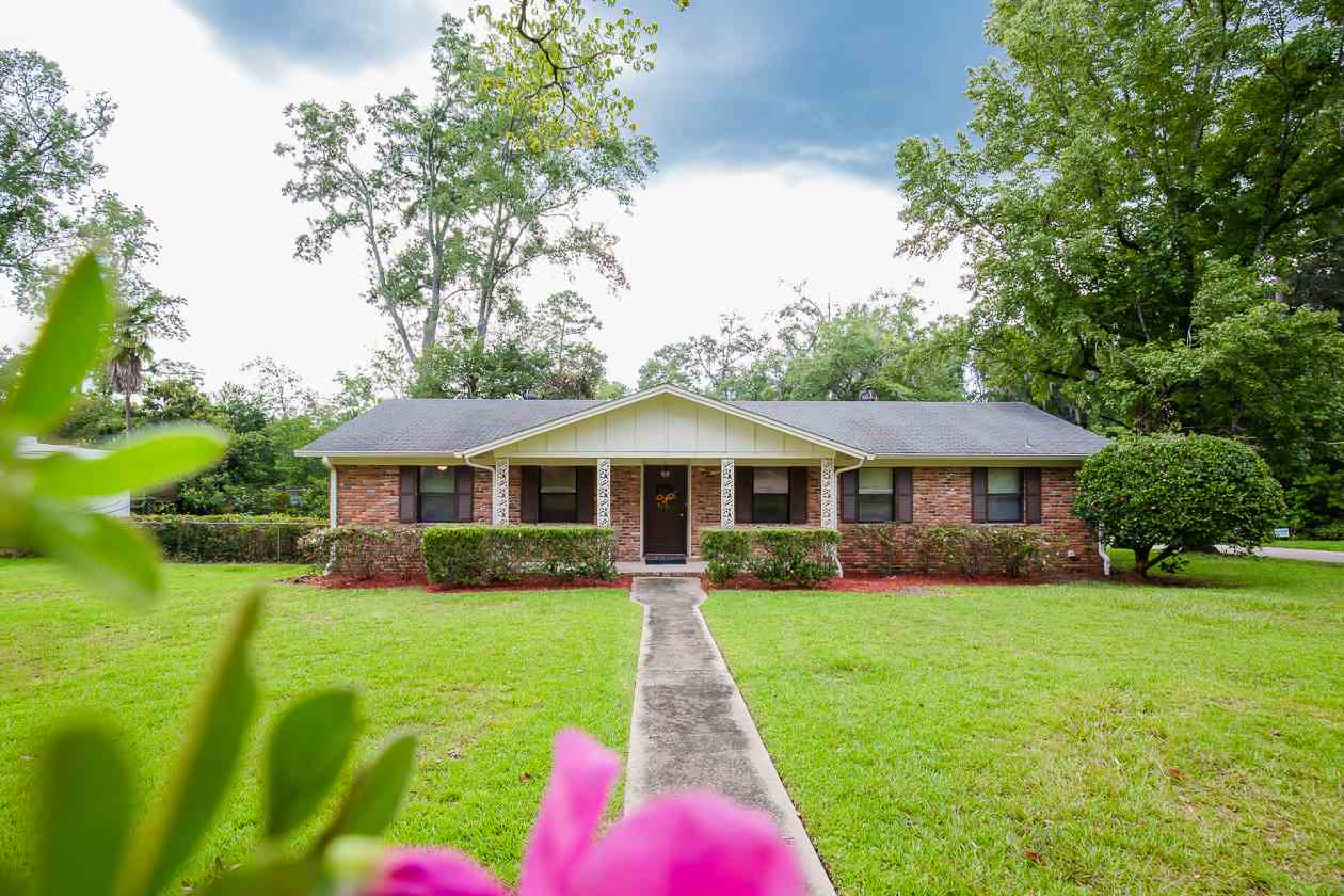 A charming brick home surrounded by a lush front yard and a vibrant flower garden, showcasing colorful blooms.