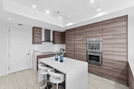 Modern kitchen with wood-grain cabinets, built-in double ovens, and a white island with bar stools.