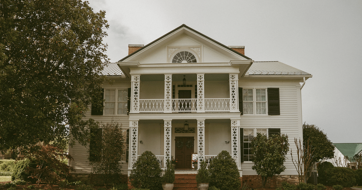 White two-story house with ornate porch columns and covered balconies on both levels.