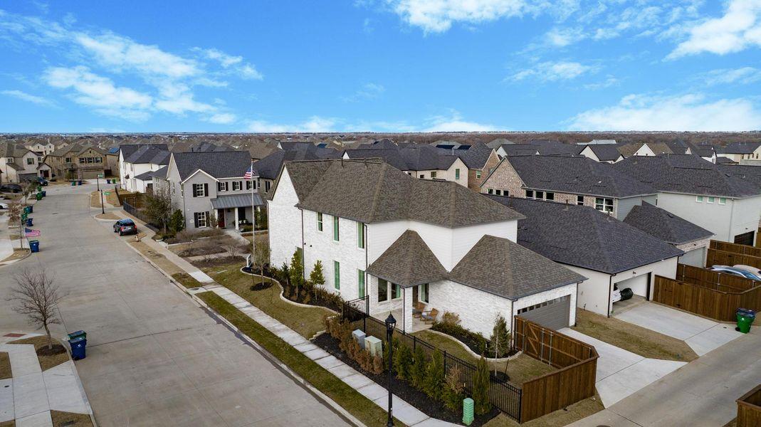 Aerial view of suburban homes along a residential street, with fenced yards and a broad blue sky.