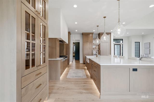 Luxury kitchen with a large white island, pale wood cabinetry, and glass pendant lights.
