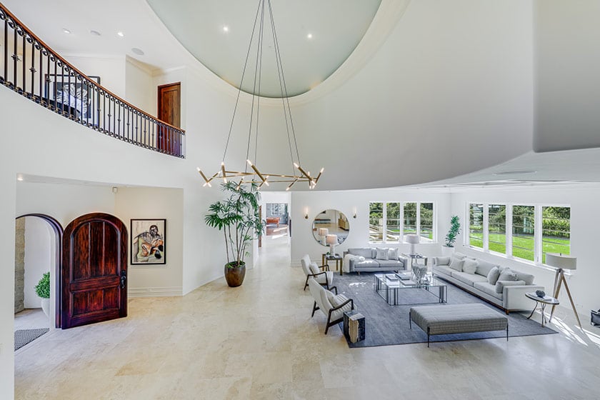 Double-height living room with modern seating, a sculptural chandelier, and windows overlooking a green lawn.