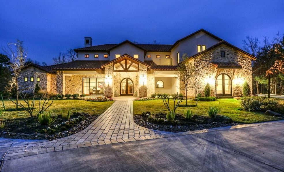 Two-story stone home at dusk with a warmly lit facade and paved front walkway.