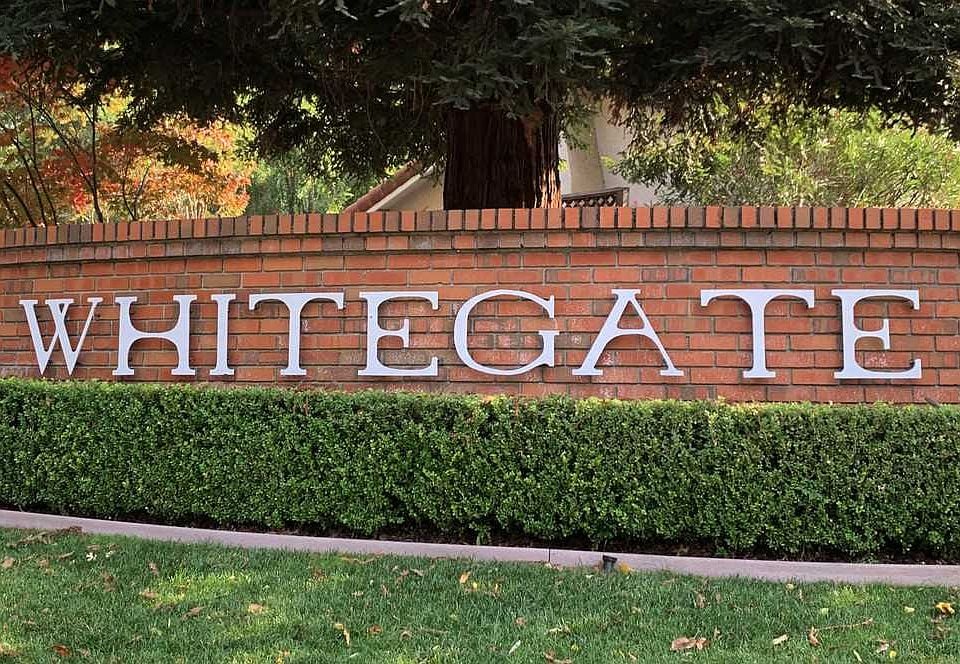 Whitegate neighborhood sign on a brick wall above a trimmed hedge.