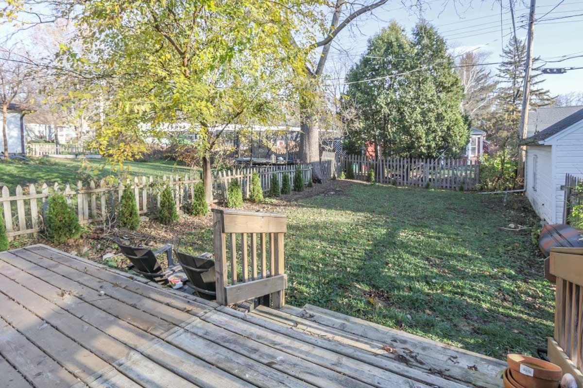 Fenced backyard with a wooden deck, lawn, outdoor chairs, and autumn trees.