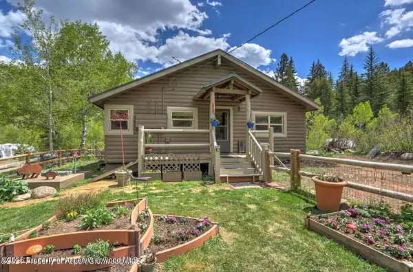 Wood-sided cabin with a covered porch, raised garden beds, and trees surrounding the yard.