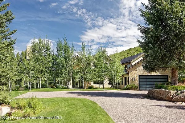 Large stone-and-wood home with a curved gravel driveway, green lawn, and mature trees.