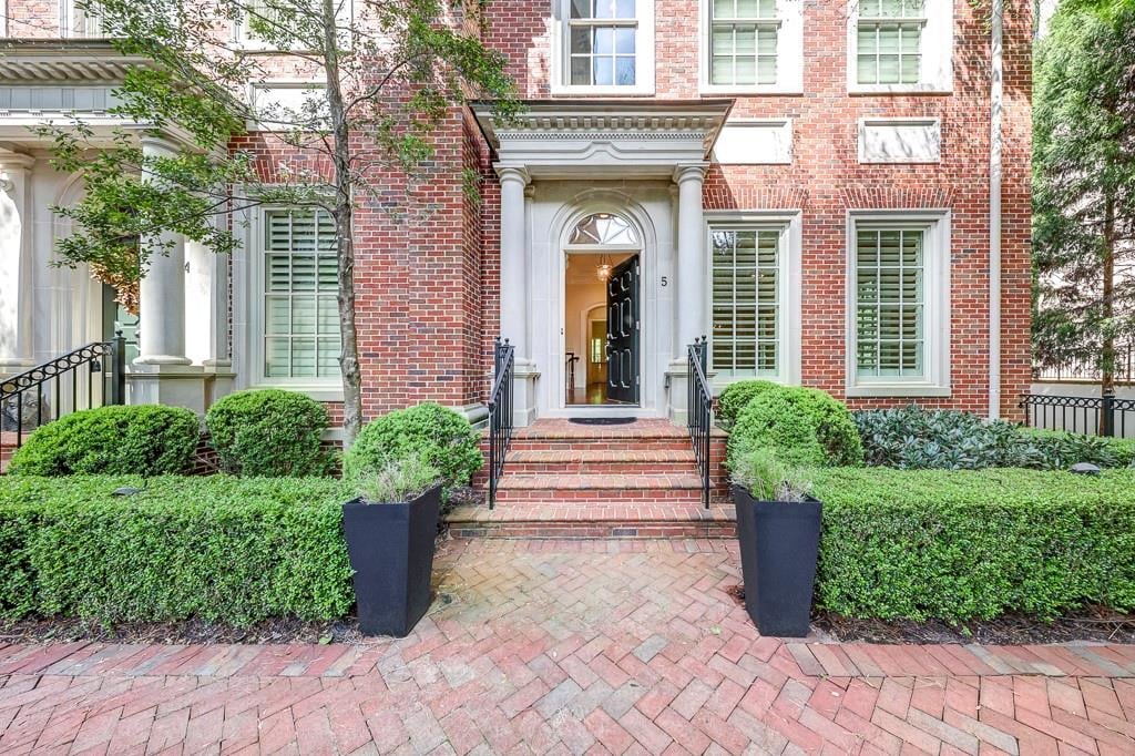 Red-brick home with a columned entry, open front door, and landscaped brick walkway.