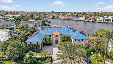 Waterfront home with a blue roof, palm trees, and a canal behind it.
