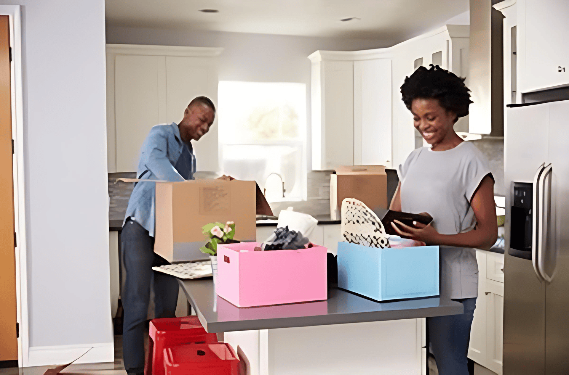 A couple packs dishes and belongings into colorful boxes in a bright kitchen.