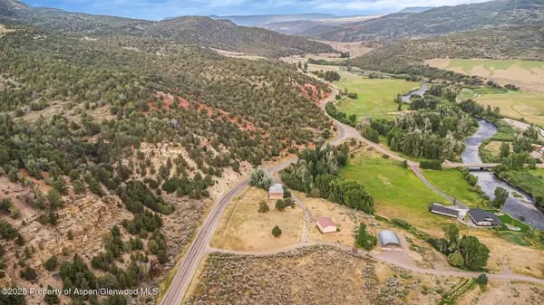 Aerial view of a rural valley with a winding river, green fields, and wooded hills.