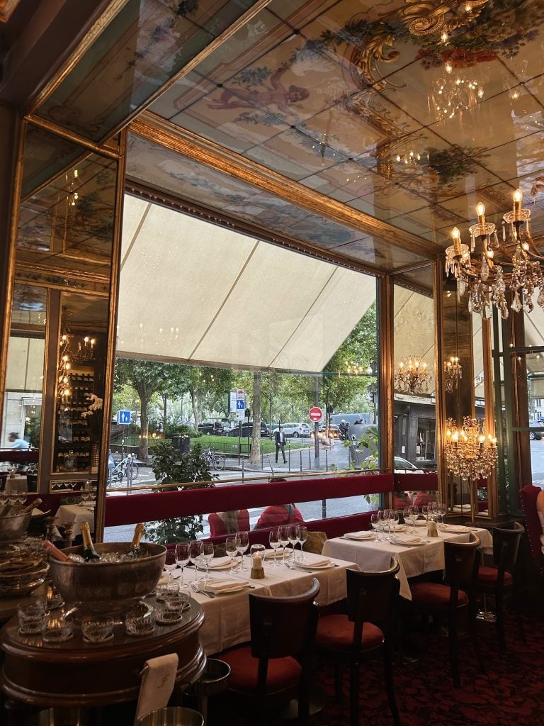 Restaurant dining room with ornate painted ceiling, crystal chandeliers, and white-tablecloth tables.