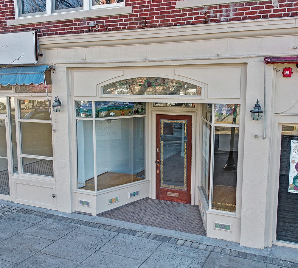 Vacant storefront with a recessed wooden door and decorative stained-glass windows.