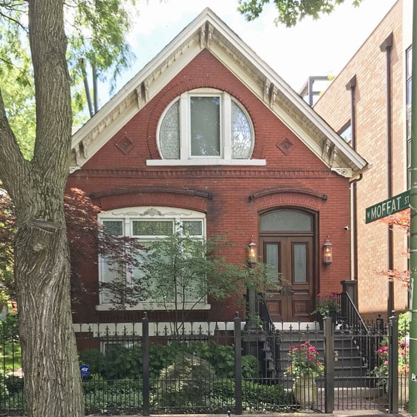 Red-brick house with a steep gable, arched entry, and iron fence.