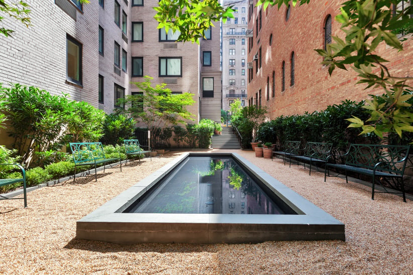 Courtyard reflecting pool between brick apartment buildings, surrounded by greenery and benches.
