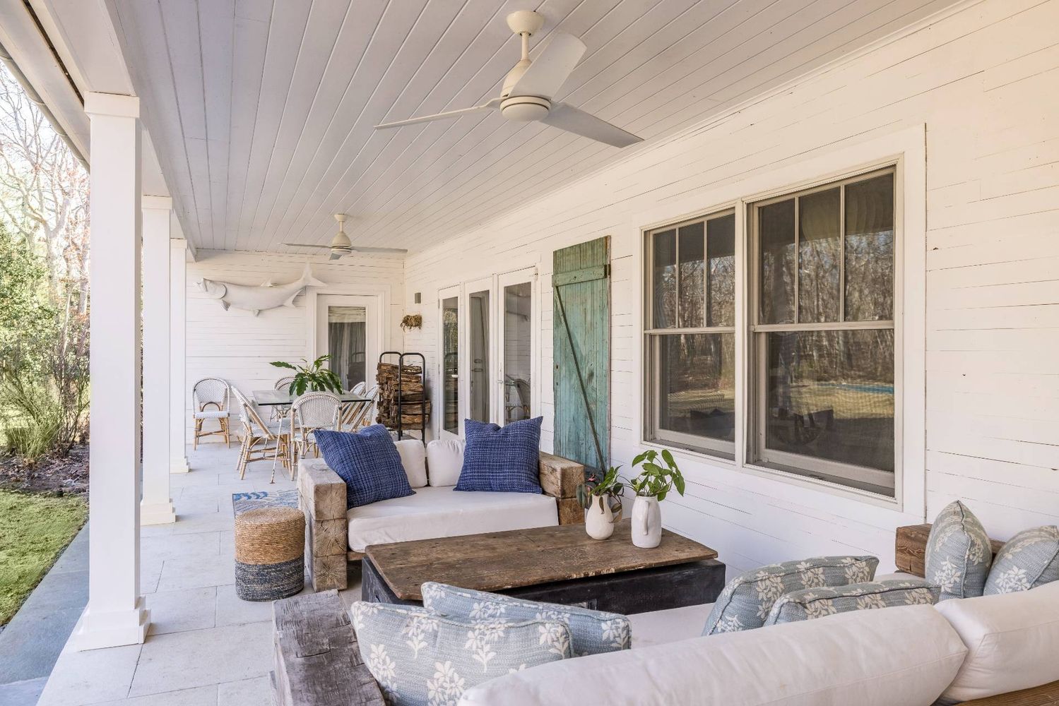 Covered porch with lounge seating, ceiling fans, and a weathered green shutter.