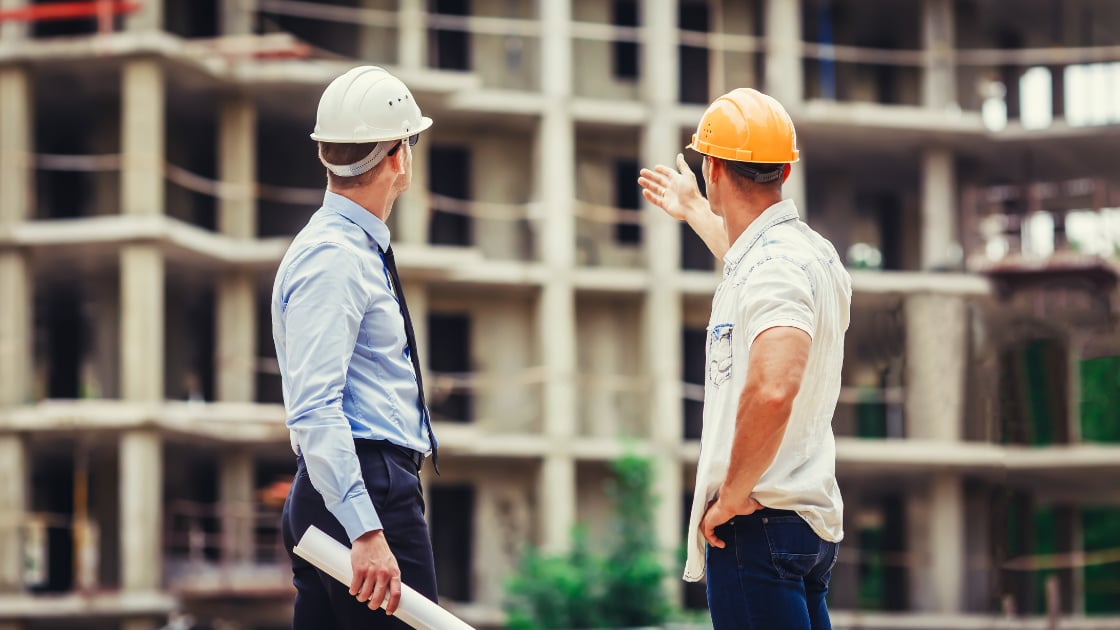 Two construction professionals discussing a new housing development site, representing the behind-the-scenes realities of buying new construction homes in Oregon.