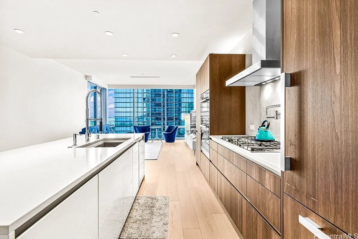 Modern condo kitchen with a long white island, wood cabinetry, and high-rise views through floor-to-ceiling windows.
