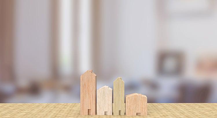 Wooden building-shaped blocks stand on a tabletop against a blurred interior.