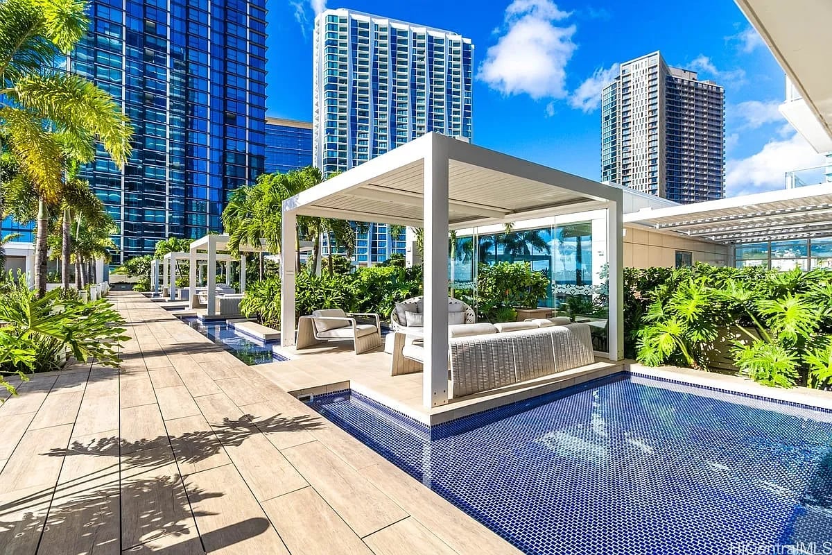 High-rise pool terrace with white cabanas, tropical plants, and city towers.