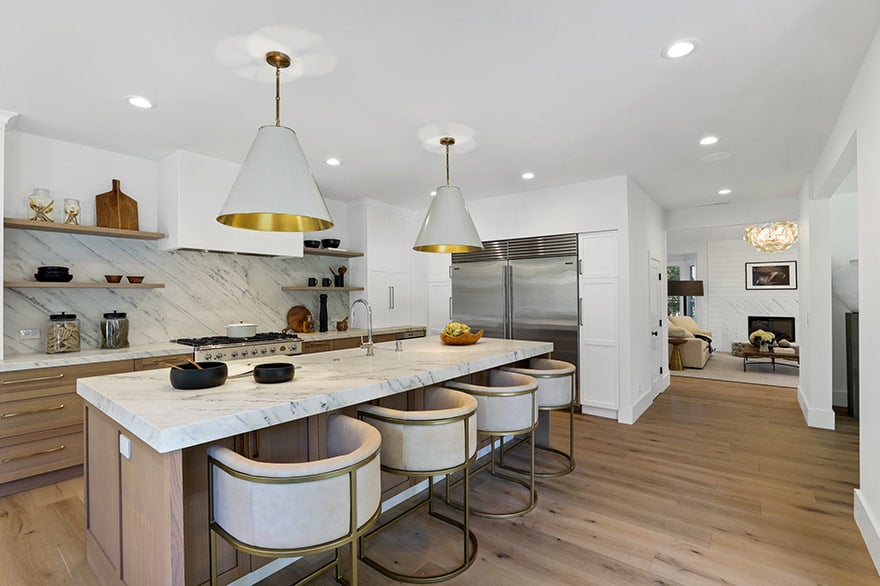 Staged kitchen with a marble island, brass-trimmed stools, and stainless steel appliances.