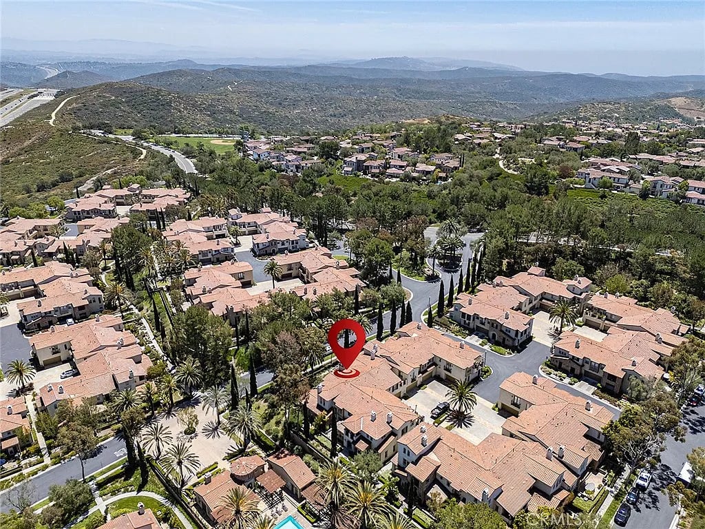 Aerial view of a terracotta-roofed neighborhood, with a red pin marking one home and hills in the distance.
