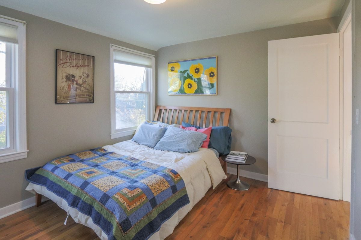Bedroom with a patchwork quilt, wooden headboard, and hardwood floors.