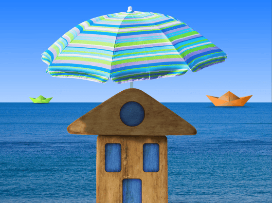 A wooden beach house beneath a striped umbrella, with paper boats floating on the ocean.