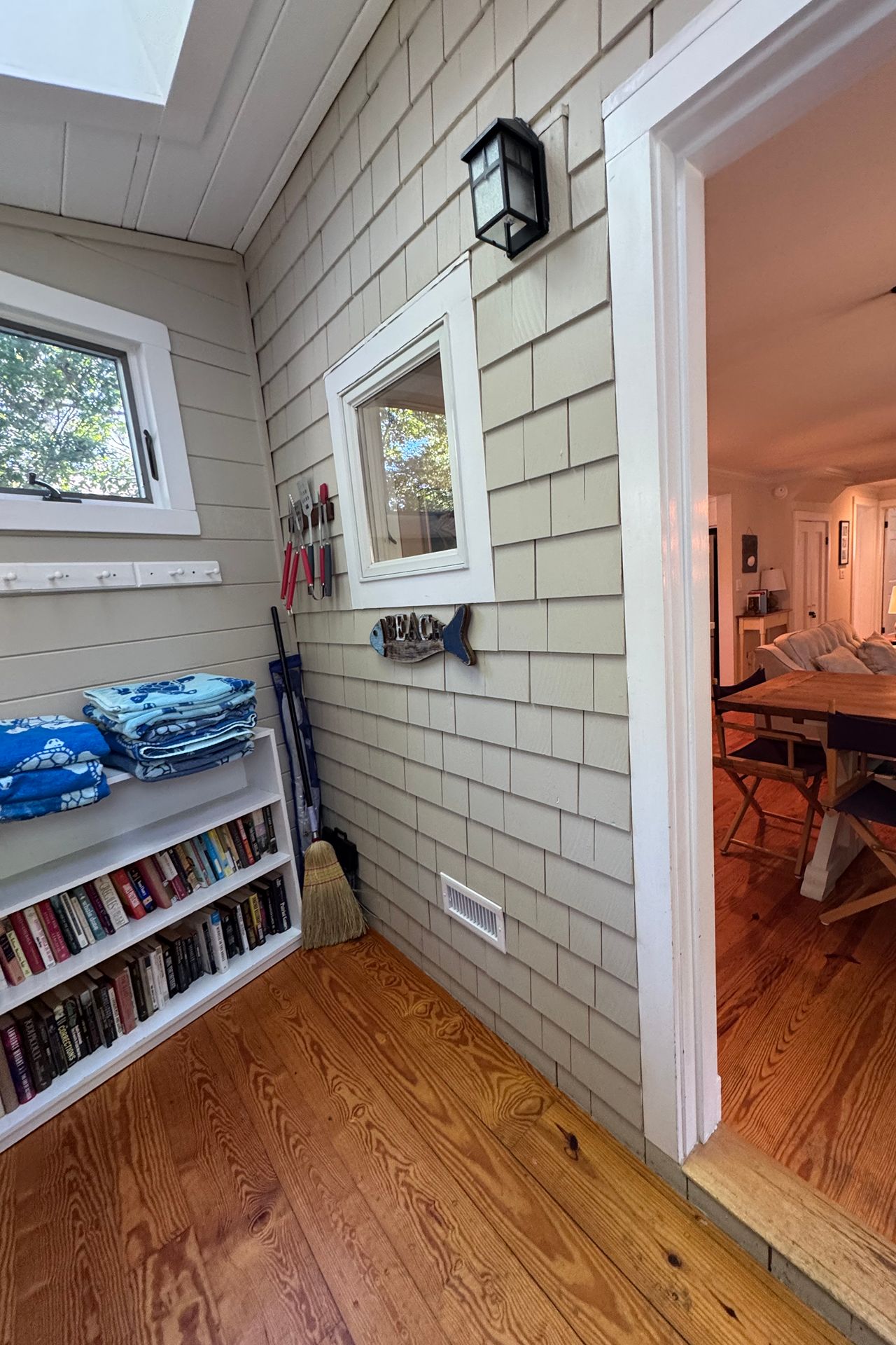 Mudroom with a built-in bookshelf, stacked beach towels, and a doorway into the living room.