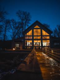 Modern lake house glowing through large windows at night, beyond a wet wooden walkway.