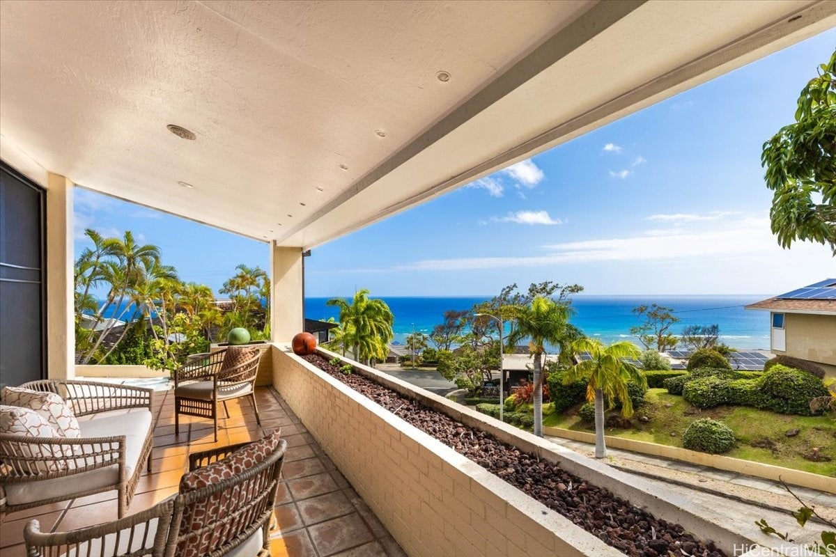 Covered lanai with wicker seating overlooking palm trees, landscaped grounds, and the ocean.