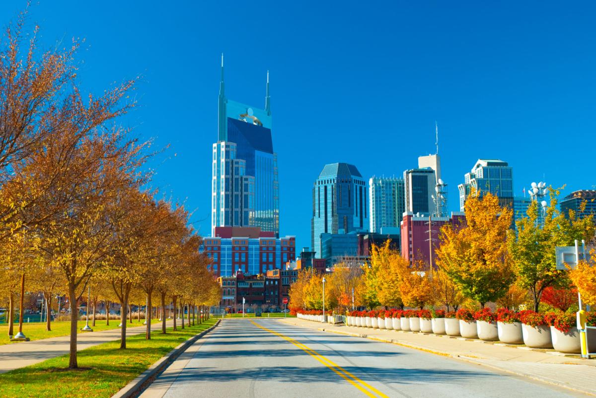Downtown Nashville skyline beyond a tree-lined street with vivid autumn foliage.
