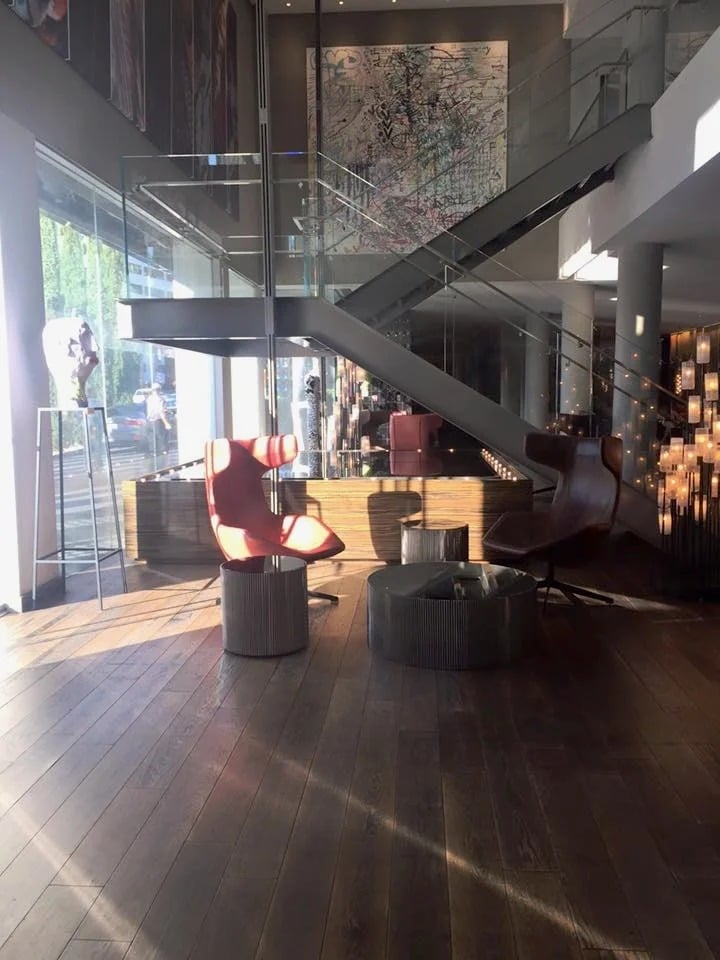 Modern hotel lobby with a glass staircase, sculptural lounge chairs, and large abstract artwork.