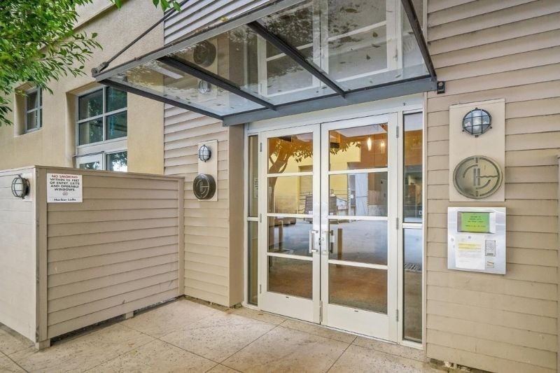 A detailed shot of the main entrance to the Harbor Lofts building, featuring double glass doors under a clear awning and exterior lighting fixtures.