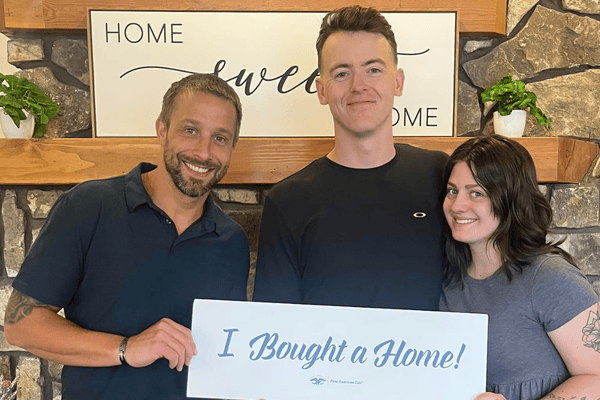 Three people celebrate a home purchase while holding an “I Bought a Home!” sign.
