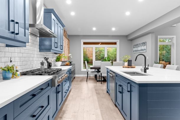 Modern kitchen with blue cabinets, white countertops, and a large island beside a dining area.