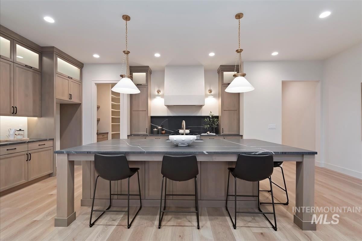 Kitchen with oversized island featuring oak cabinets, black leather granite counter and milk glass pendant lights