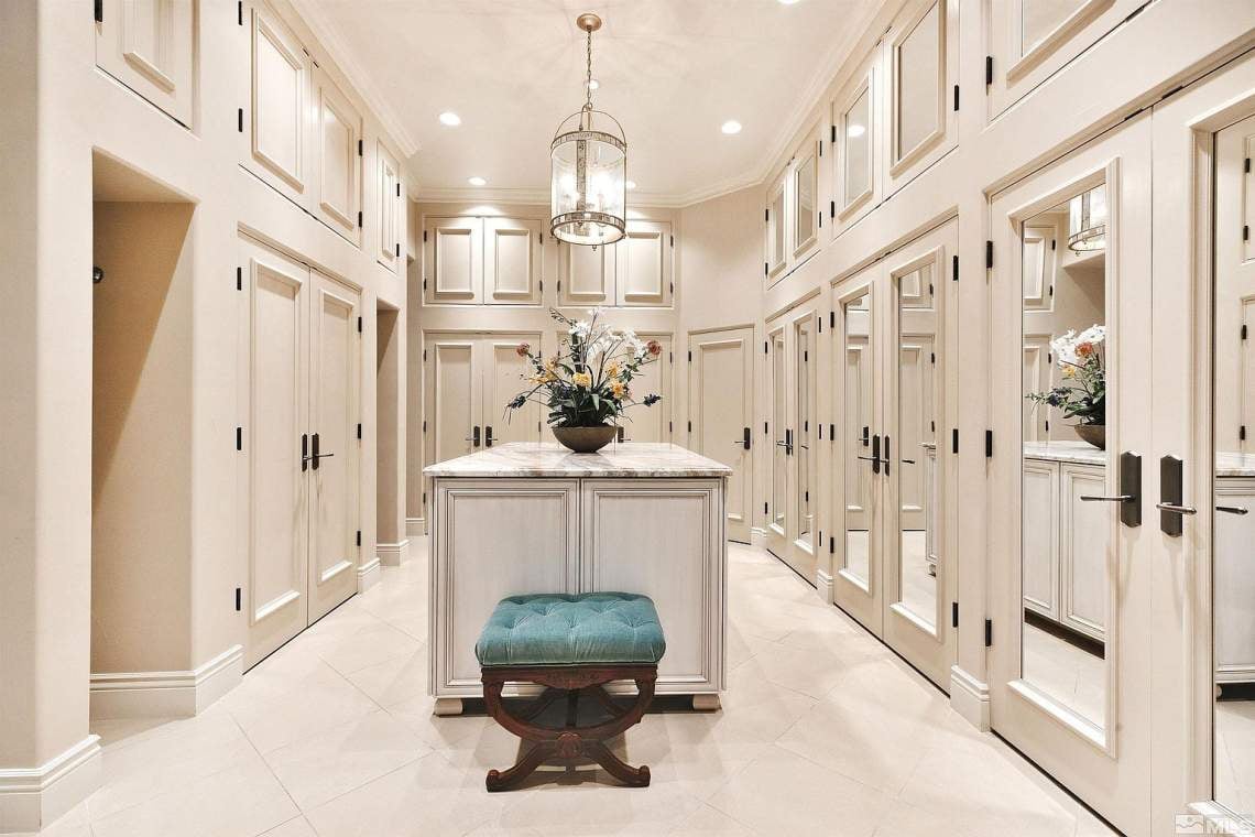 Walk-in closet with mirrored cabinetry, a central island, and a teal upholstered stool.