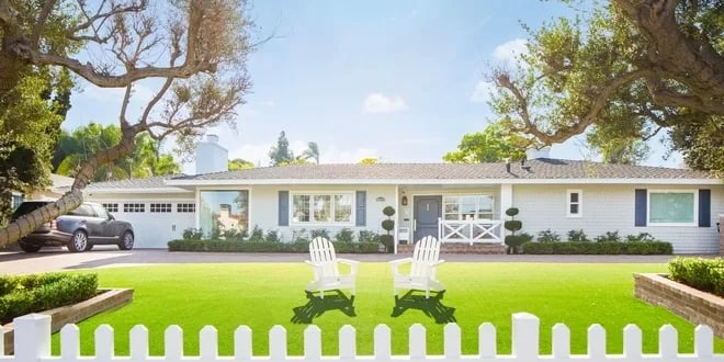 Single-story ranch home with a wide garage, covered porch, green lawn, and white picket fence.