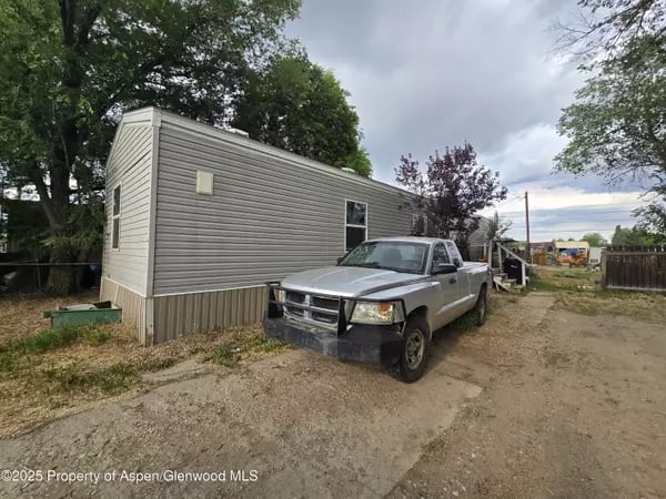 Manufactured home with gray siding and a silver pickup parked beside it on a gravel drive.