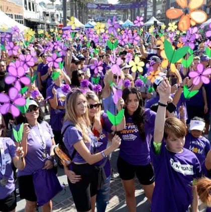 Crowd at an Alzheimer's awareness walk holding colorful flower-shaped pinwheels.