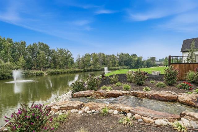 Landscaped pond with fountains, stone edging, flower beds, and a deck at the right.