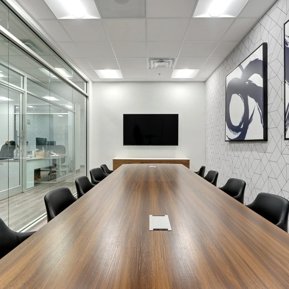 Conference room with a long wood table, black chairs, glass partitions, and abstract wall art.