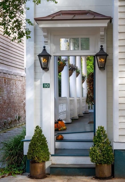 White house entrance with columned porch, black lanterns, and pumpkins by the steps.