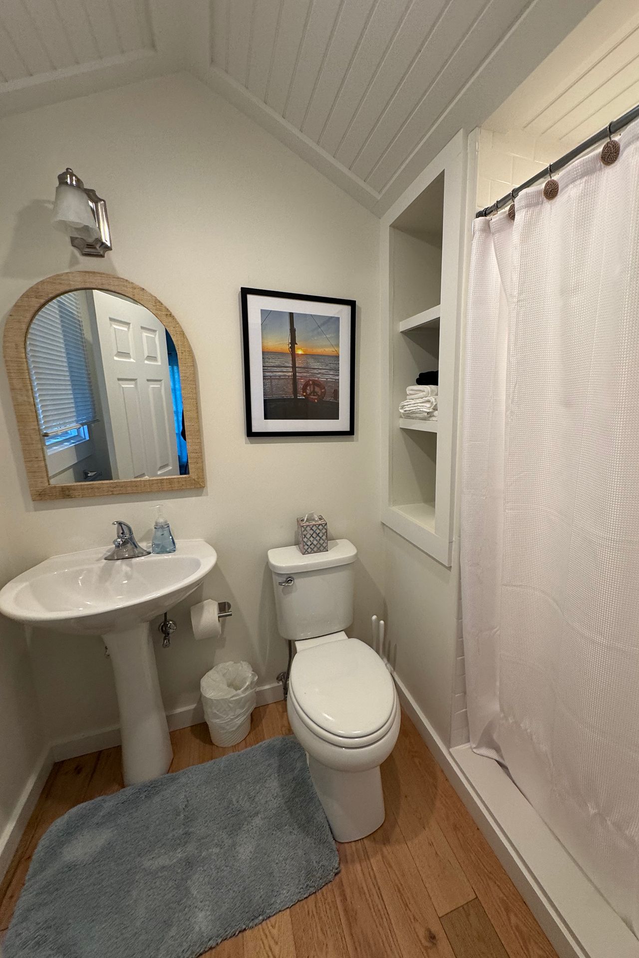 Bathroom with a pedestal sink, toilet, built-in towel shelves, and a shower behind a white curtain.